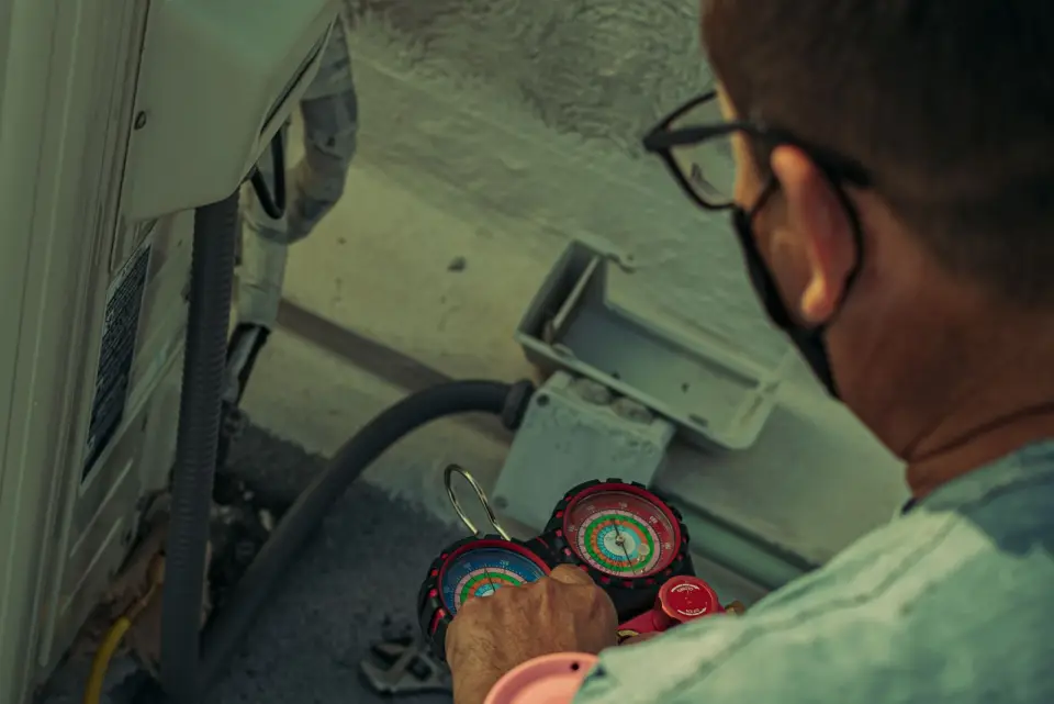 Technician servicing an outdoor air conditioning unit with gauges connected